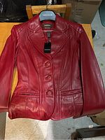 Front view of the red leather jacket laid flat, showing buttons and lapel details