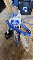 Front view of blue pump unit with Graco label and coiled blue hose and clear suction tube visible