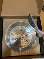Open box showing new Henckels stainless steel steamer basket with user instructions inside.