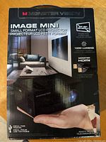 Front of the boxed Monster Vision Image Mini projector showing branding and key features such as 1000 lumens and HDMI compatibility.