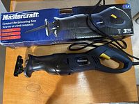 Compact reciprocating saw laid on table alongside its original box showing product name, image, and branding.