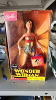 Front view of boxed Wonder Woman Barbie doll with accessories visible inside.