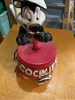 Front view of ceramic Pepe Le Pew cookie jar holding red cookie jar with 'COOKIES' text.
