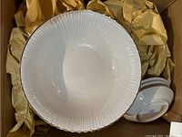 Set of white porcelain plates with ribbed texture and gold rim, stacked and displayed in box with packaging paper.