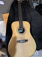 Natural wood finish acoustic guitar with six strings, one string broken, lying in soft case.
