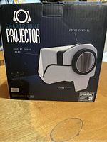 Closed box of smartphone projector showing branding, focus control, and phone insertion area.