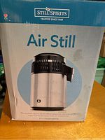 Box front showing product name 'Air Still' with image of stainless steel distiller and 4L capacity noted.