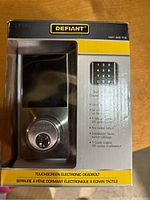 Front view of the Defiant touchscreen electronic deadbolt lock in original box showing model and features.