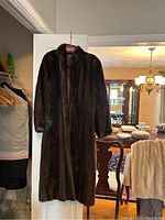 Darker long brown fur coat hanging on door, background shows dining room
