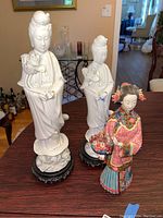 3 Asian themed figurines on wooden table showing white porcelain and colorful clay pieces