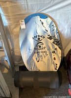 Balance board and roller set leaning against a white tarp or wall in a garage environment, showing the front design and general condition.