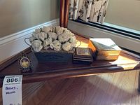Wide shot of two decorative boxes, faux flower arrangement in GreenThumb Seed Plant Company container, and small framed miniature portrait on a wooden table.