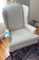 Front view of cream wingback chair highlighting patterned upholstery and wooden cabriole legs on Persian style rug