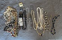 Image showing a large collection of various necklaces, bracelets, and earrings arranged on a quilted surface, including black, pearl, and red beaded pieces and multiple earrings on cards.