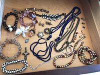 Overview photo showing multiple necklaces, pins, earrings, and bracelets on a wood drawer surface