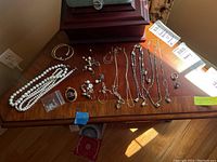Wide view of the costume jewelry spread out on a wooden surface showing most items including necklaces, rings, bracelets, earrings, and a brooch.