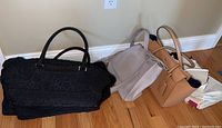Three handbags (black, grey, tan) on hardwood floor