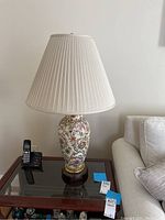 Full view of the lamp on a glass table next to a sofa, showing the entire lamp with shade and its surroundings.