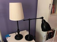 Two table lamps on a white surface against a purple wall, showing their full profile.