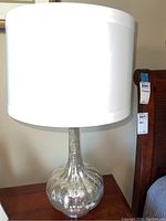 Full view of one lamp showing the silver mercury glass base and white drum shade.