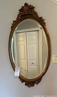 Full view of the gold-toned oval mirror hanging on a wall, showing its size and shape.