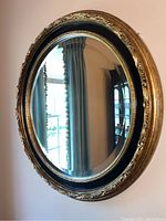 Frontal view of round mirror showing beveled glass and ornate gold frame with black inner trim.