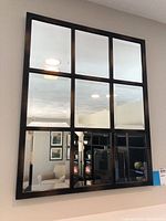 Full front view of the window pane mirror showing nine reflective panes within a dark frame, reflecting furniture and ceiling lights in the room.