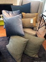 Seven decorative throw pillows in various colors and fabrics displayed on a chair and floor.