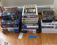 Photo showing multiple stacks of puzzle boxes including 500, 750, and 1000 piece sets on a wooden floor.