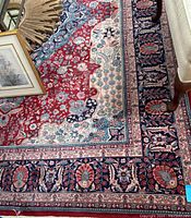 Corner view showing red field, cream and navy floral motifs, partial furniture legs
