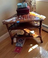 Full view of triangular wooden side table with contents on top and shelves. The table surface holds assorted jewelry, boxes, and other small items (not included). Two wooden shelves below display decorative items and small boxes.