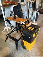 Black and Decker work bench with wooden top, two-tier yellow and black toolbox, Rigid Kwik Spin plumbing tool packaging, and plumbing accessories.