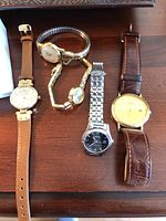 Five untested wristwatches laid out on a wooden surface showing diverse styles and bands.