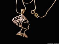 Front close-up of the Nefertiti pendant and chain clasp on black background showing texture and mark details.