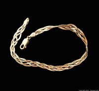 Gold braided herringbone bracelet laid flat on black background showing lobster clasp and braided design