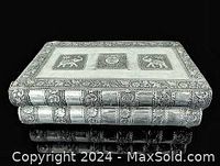 Closed jewelry box shaped like a book showing embossed metal top with three rectangular design panels and detailed border.