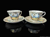 Two vintage Colclough teacup and saucer sets featuring the Lady in Garden colorful decal. Both cups show detailed garden scenes with a lady figure, paired with matching saucers.
