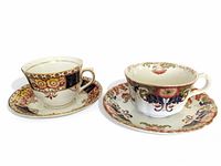 Two vintage teacups and matching saucers with floral decorative patterns placed side by side on a white background.