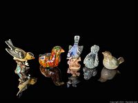 Front view of five vintage ceramic bird figurines arranged in a row on reflective black surface, showing detailed glazes and various bird species.