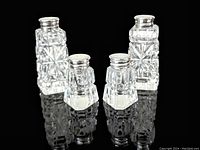 Front view of two pairs of crystal salt and pepper shakers with sterling silver caps, showing the faceted cut crystal and reflective caps.