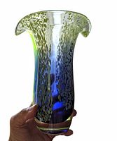 Hand holding vintage 8 inch tall hand blown glass vase with flared lip, speckled lime green and cobalt blue colors.
