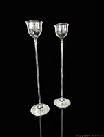 Pair of tall silver plate BIRKS St. James candlesticks with tulip-shaped holders, standing upright on a dark reflective surface.