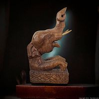 Side view of vintage carved solid wood elephant bookend showing the elephant trunk raised and base carving details in natural wood finish.