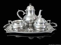 Front view of tea pot, creamer, sugar bowl, tray, tongs and spoon arranged on tray