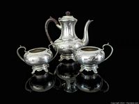 Front view of the three-piece pewter tea set comprising a teapot, creamer, and sugar bowl on a reflective black surface