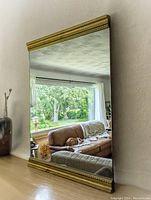Mirror mounted on a wall showing reflections of a living room with large window and couch.