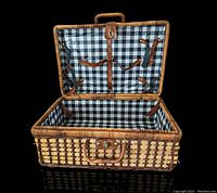 Open view of woven picnic basket, showing blue and white checkered vinyl interior lining and multiple leather securing straps inside.