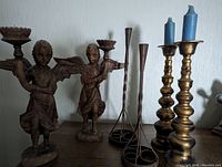 Full set of six candlestick holders displayed together showcasing assorted materials and styles including brass, metal, and carved wood