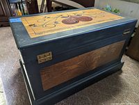 Side view of wooden chest showing hand painted natural wood panel and dark blue painted surrounding areas