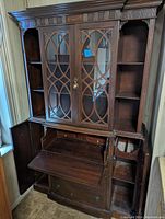 Front view of hideaway desk with bookcase hutch showing open fold-down desk surface, glass cabinet doors with lattice, and side open shelves.